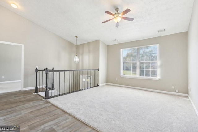 empty room featuring hardwood / wood-style flooring, ceiling fan, a textured ceiling, and vaulted ceiling