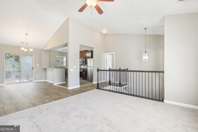 carpeted spare room featuring lofted ceiling and ceiling fan with notable chandelier