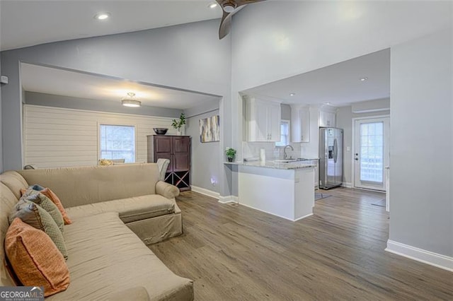 living room featuring ceiling fan, lofted ceiling, sink, and light hardwood / wood-style flooring