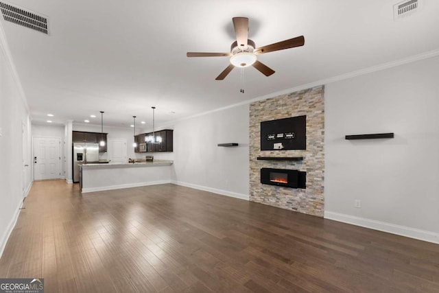 unfurnished living room featuring ceiling fan with notable chandelier, dark hardwood / wood-style floors, a stone fireplace, and ornamental molding