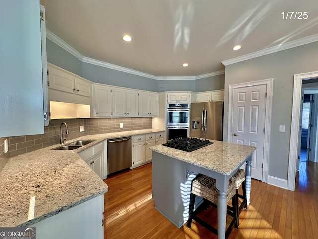 kitchen with a center island, white cabinets, sink, light stone countertops, and appliances with stainless steel finishes