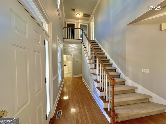 stairway featuring wood-type flooring, a towering ceiling, and crown molding