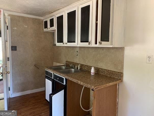 kitchen with sink, dark wood-type flooring, a textured ceiling, white cabinets, and ornamental molding