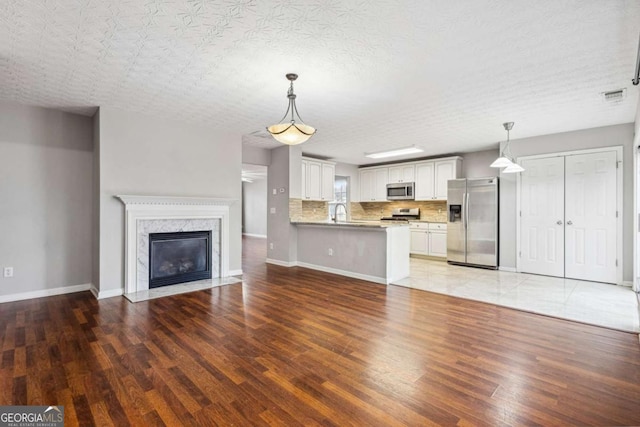 unfurnished living room featuring light wood-style flooring, visible vents, baseboards, and a high end fireplace