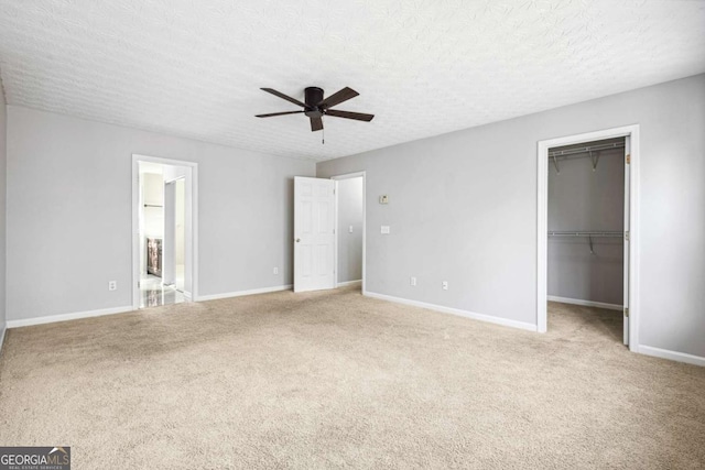 unfurnished bedroom with carpet, a textured ceiling, ceiling fan, a spacious closet, and connected bathroom