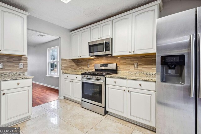 kitchen featuring white cabinets, stainless steel appliances, and light stone counters