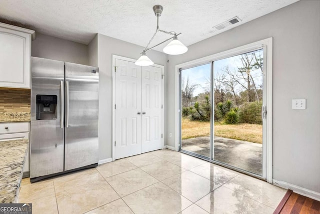 kitchen with white cabinets, hanging light fixtures, stainless steel fridge, light stone countertops, and tasteful backsplash