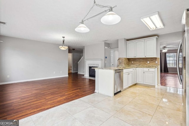 kitchen with kitchen peninsula, light stone countertops, appliances with stainless steel finishes, decorative light fixtures, and white cabinetry