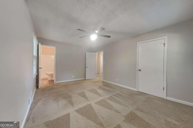 unfurnished bedroom featuring ensuite bath, ceiling fan, a textured ceiling, light colored carpet, and a closet