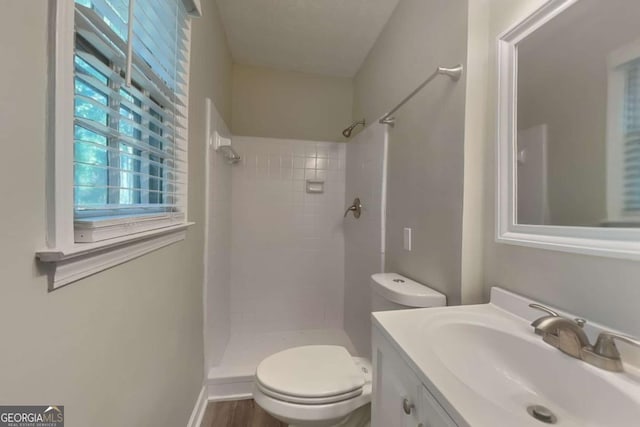 bathroom with a tile shower, vanity, toilet, and wood-type flooring