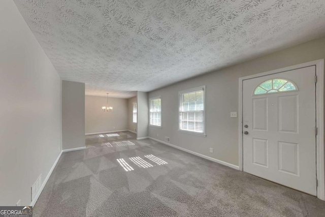 carpeted entrance foyer featuring a textured ceiling and an inviting chandelier