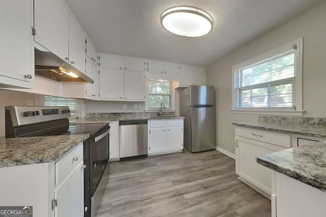 kitchen featuring sink, light stone counters, light hardwood / wood-style flooring, white cabinets, and appliances with stainless steel finishes