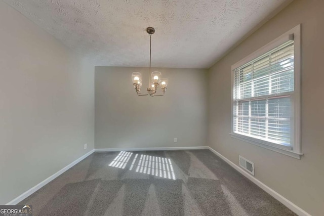 carpeted spare room with a chandelier and a textured ceiling