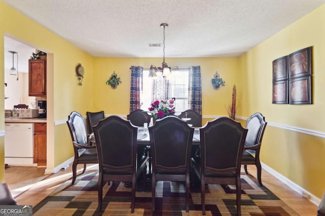 dining space with wood-type flooring, a textured ceiling, and a notable chandelier