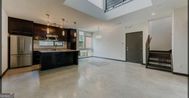 kitchen featuring stainless steel fridge, dark brown cabinetry, sink, hanging light fixtures, and an island with sink