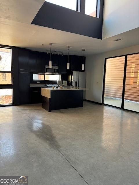 kitchen featuring sink, a towering ceiling, pendant lighting, a center island with sink, and appliances with stainless steel finishes