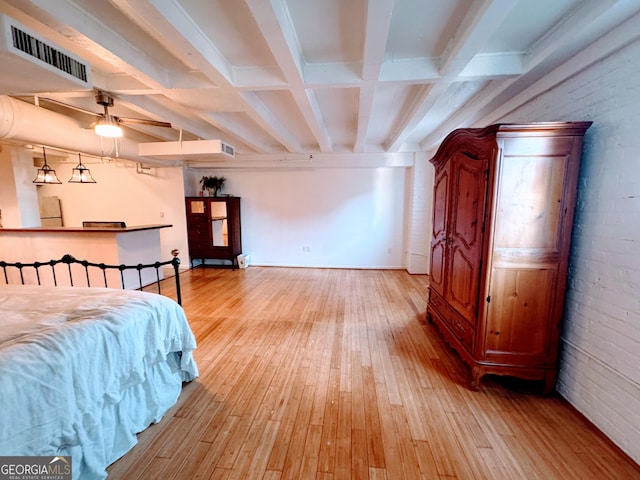 bedroom with beam ceiling, light wood-type flooring, white refrigerator, and brick wall