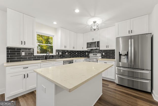 kitchen with sink, a kitchen island, light stone counters, white cabinets, and appliances with stainless steel finishes