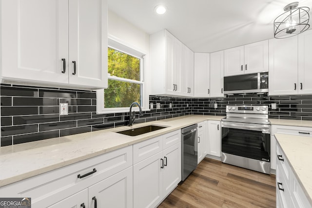 kitchen with sink, dark hardwood / wood-style floors, appliances with stainless steel finishes, decorative light fixtures, and white cabinetry