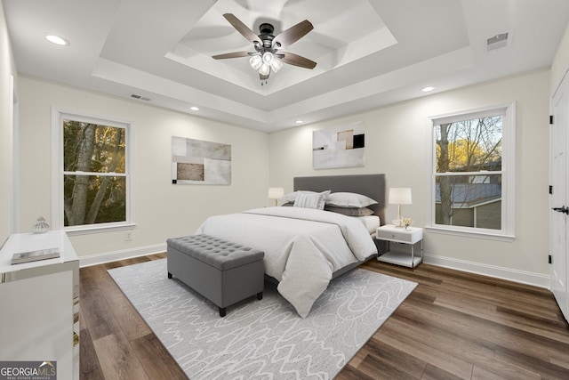 bedroom with ceiling fan, dark wood-type flooring, and a tray ceiling