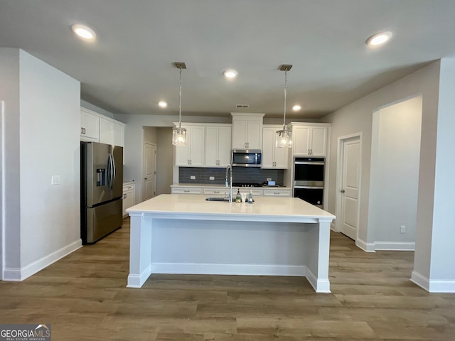 kitchen featuring sink, backsplash, stainless steel appliances, white cabinets, and decorative light fixtures