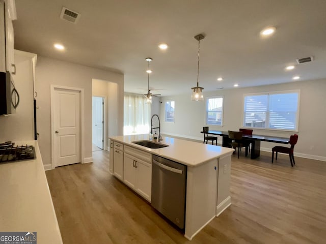 kitchen featuring appliances with stainless steel finishes, decorative light fixtures, white cabinetry, sink, and a center island with sink