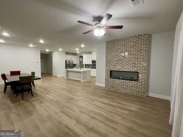 living room with ceiling fan, sink, a fireplace, and light wood-type flooring