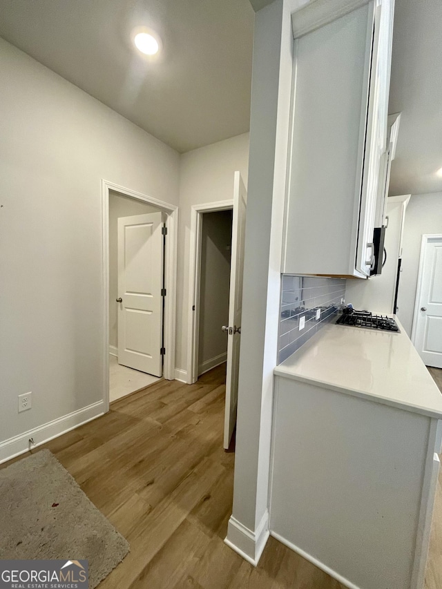 kitchen with tasteful backsplash, white cabinetry, stainless steel gas cooktop, and light wood-type flooring