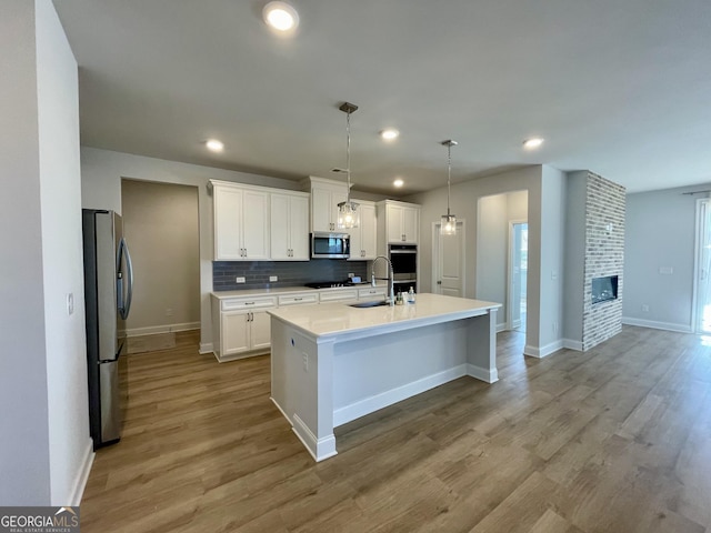 kitchen featuring pendant lighting, an island with sink, white cabinets, and appliances with stainless steel finishes