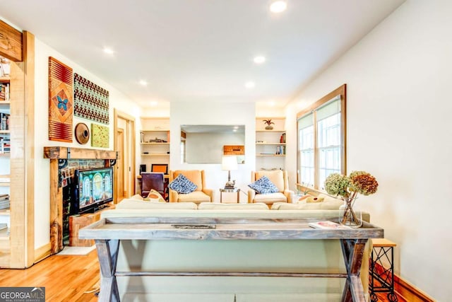 living room with a fireplace, built in shelves, and light wood-type flooring