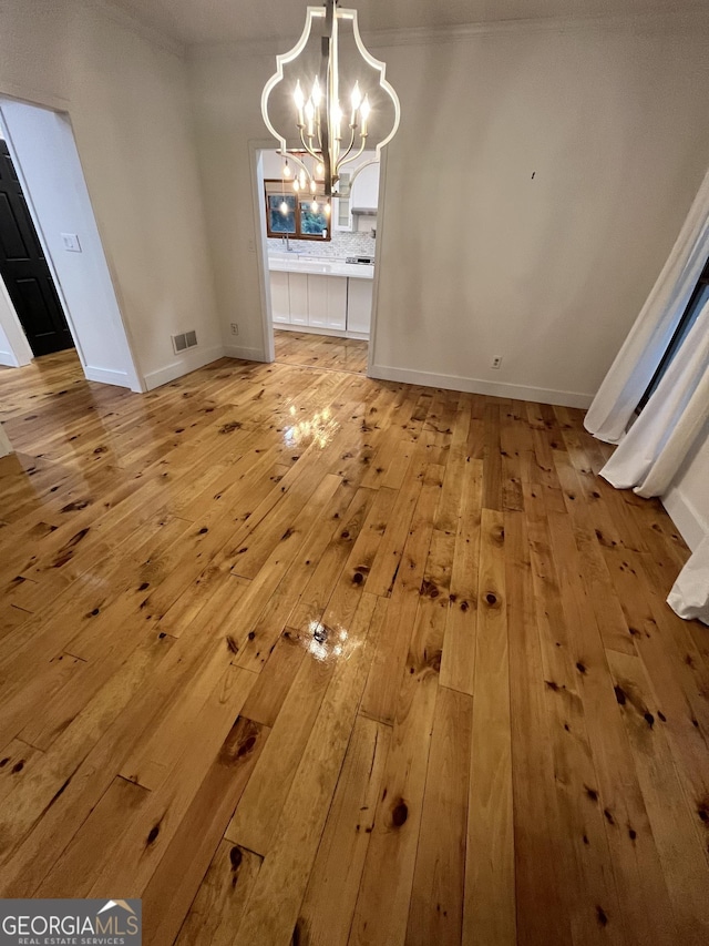 unfurnished dining area featuring a notable chandelier, light hardwood / wood-style floors, and ornamental molding