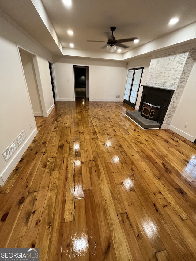 unfurnished living room featuring a wood stove, ceiling fan, and hardwood / wood-style flooring