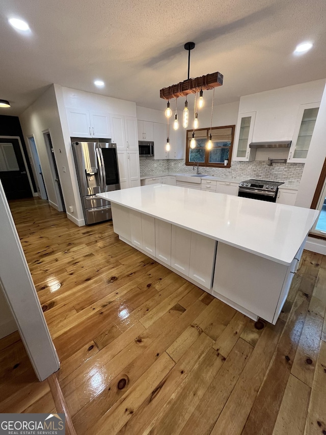 kitchen with pendant lighting, a center island, hardwood / wood-style flooring, white cabinetry, and stainless steel appliances