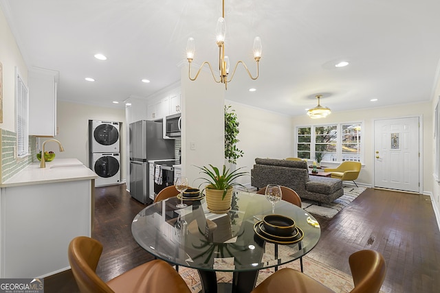 dining room featuring dark wood-type flooring, stacked washing maching and dryer, a chandelier, and sink