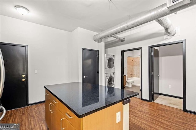 kitchen featuring a center island, stacked washer and dryer, dark stone counters, and dark wood-type flooring