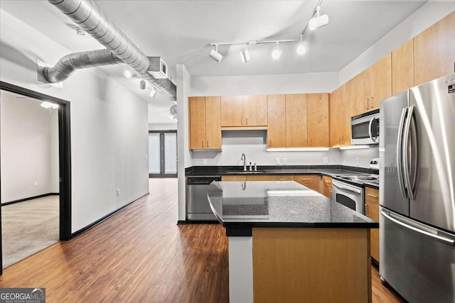 kitchen featuring sink, stainless steel appliances, dark hardwood / wood-style flooring, dark stone counters, and a kitchen island