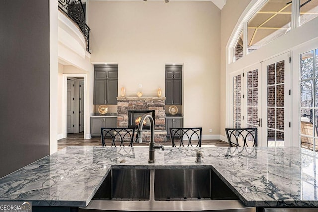 kitchen featuring sink, dark wood-type flooring, a high ceiling, a stone fireplace, and light stone counters