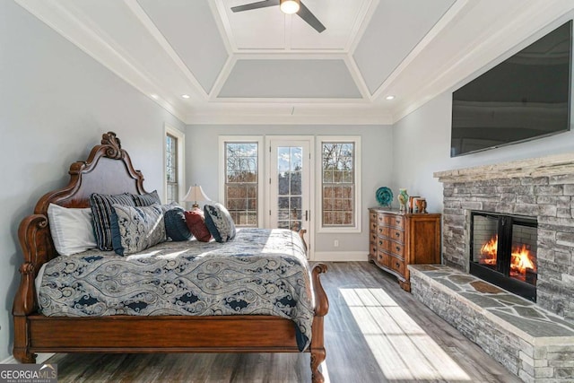 bedroom with ceiling fan, a stone fireplace, ornamental molding, and dark wood-type flooring