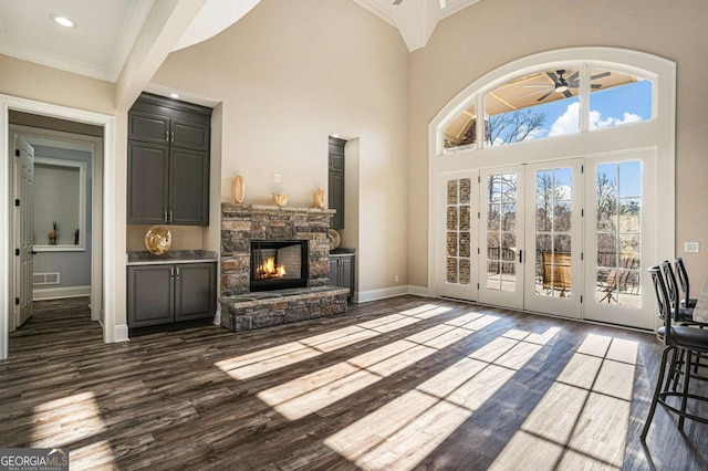 unfurnished living room with french doors, ceiling fan, dark wood-type flooring, crown molding, and a fireplace