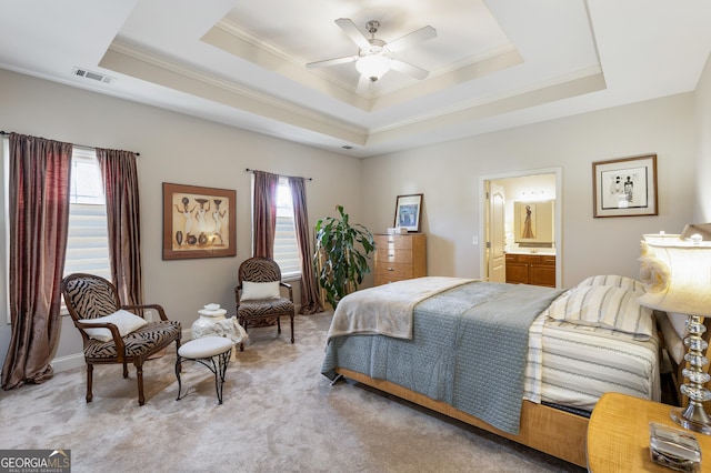 bedroom featuring ceiling fan, a raised ceiling, ensuite bathroom, light colored carpet, and ornamental molding