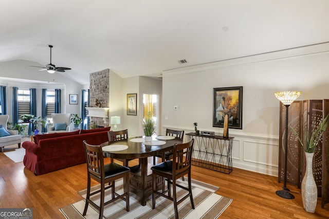 dining area featuring lofted ceiling, a stone fireplace, crown molding, hardwood / wood-style flooring, and ceiling fan