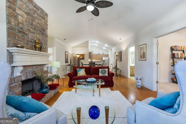 living room with ceiling fan, a fireplace, vaulted ceiling, and light wood-type flooring