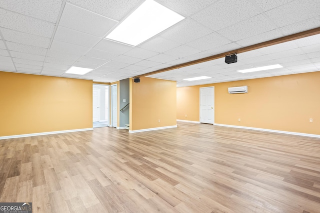 basement featuring a wall mounted air conditioner, light hardwood / wood-style floors, and a drop ceiling