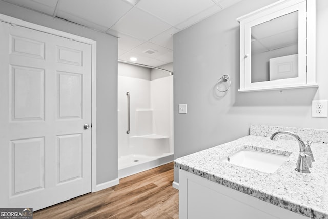 bathroom with wood-type flooring, a drop ceiling, walk in shower, and vanity