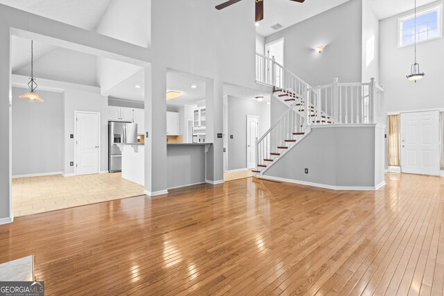 unfurnished living room with a high ceiling, ceiling fan, and light hardwood / wood-style flooring