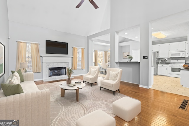 living room featuring a premium fireplace, light wood-type flooring, a healthy amount of sunlight, and lofted ceiling