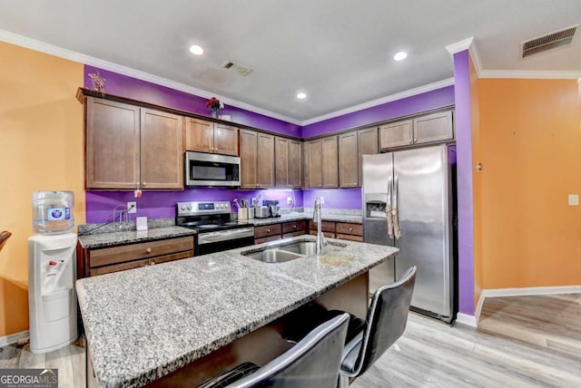 kitchen with light stone counters, ornamental molding, stainless steel appliances, a kitchen island with sink, and sink