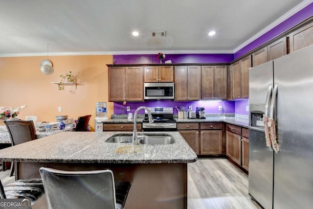 kitchen featuring sink, hanging light fixtures, stainless steel appliances, light stone counters, and light hardwood / wood-style flooring