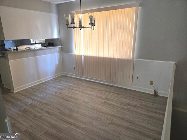 unfurnished dining area with wood-type flooring and a chandelier