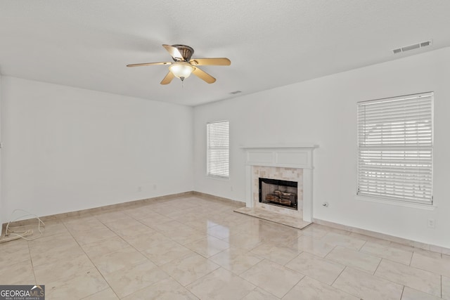 unfurnished living room featuring a textured ceiling, ceiling fan, and a tiled fireplace